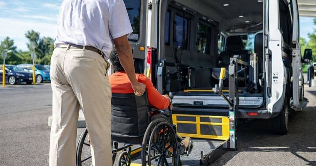 A Karing Hands driver assisting a rider in a wheelchair onto the lift of a wheelchair-accessible transport van